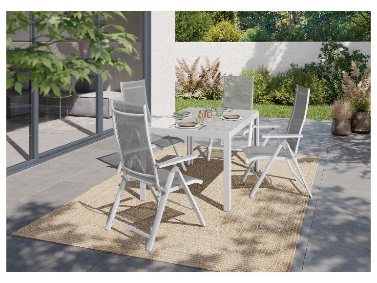 Garten-Essgruppe mit weißem Tisch und Stühlen auf einem gewebten Teppich, umgeben von Grün.