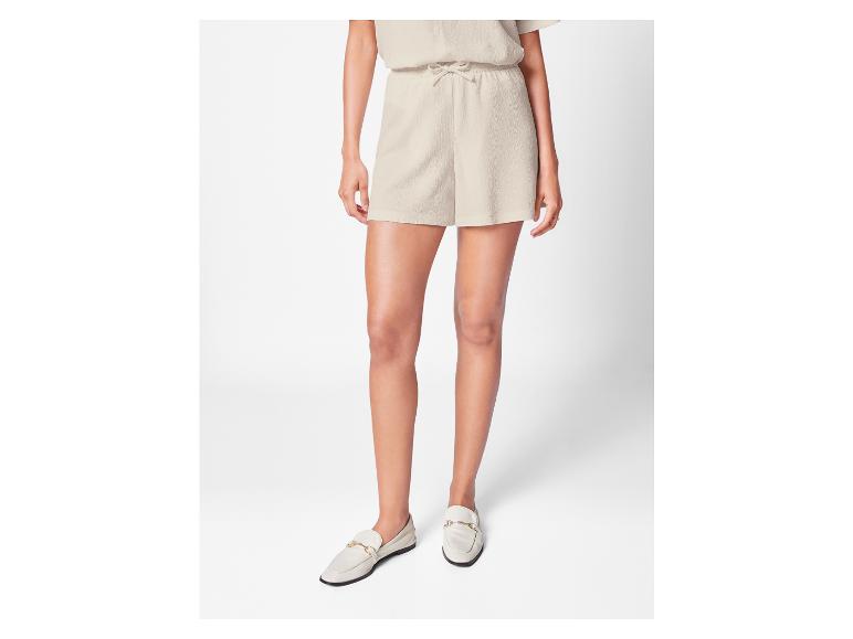 Eine Frau trägt kurze Hosen und weiße Loafer mit goldenen Ketten.