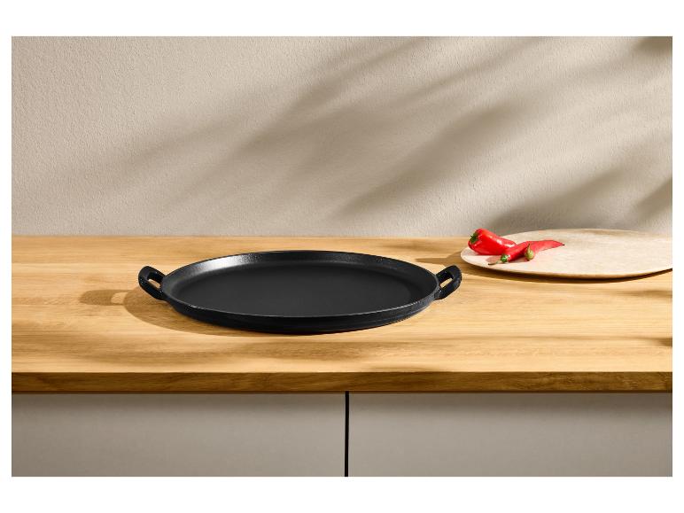 Schwarze runde Gusseisenpfanne auf einem Holztisch mit roten Paprika.