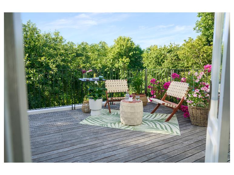 Balkon mit Holzboden, zwei Klappstühlen, einem Tisch und Pflanzen.