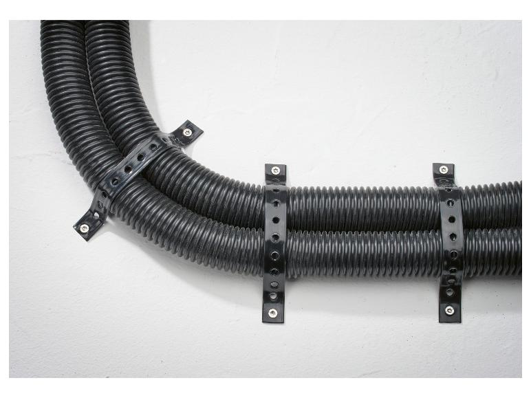 Zwei schwarze flexible Leitungen mit Kabelbindern an einer weißen Wand befestigt.