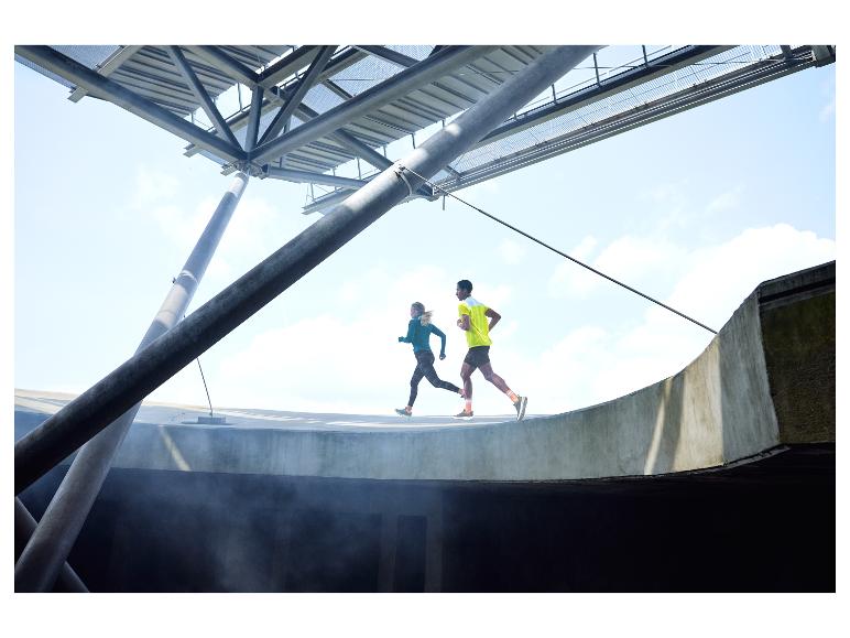 Zwei Läufer trainieren auf einer geschwungenen Strecke unter einer Metallkonstruktion.