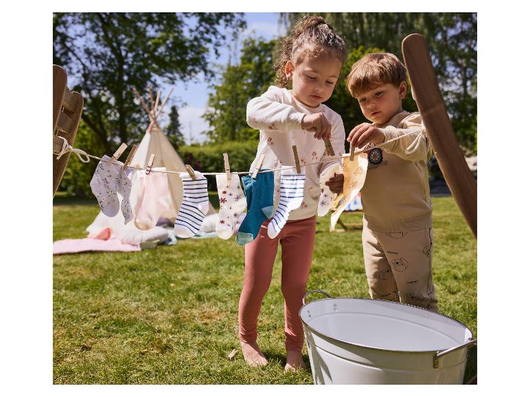Zwei Kinder hängen bedruckte Socken an eine Wäscheleine im Freien auf.