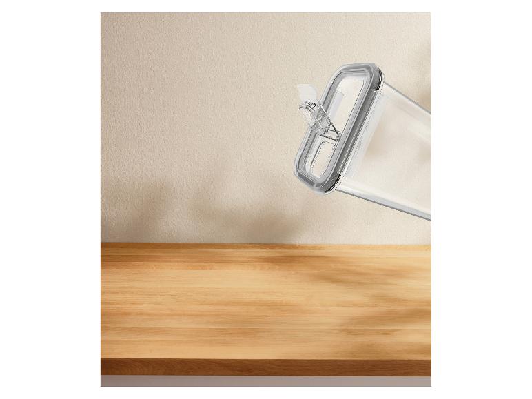 Transparenter Lebensmittelbehälter mit grauem Deckel, schräg vor einer beigen Wand und Holzoberfläche.