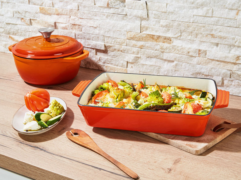 Eine orangefarbene gusseiserne Auflaufform mit einem vegetarischen Gericht aus Zucchini, Tomate, Brokkoli und Feta.