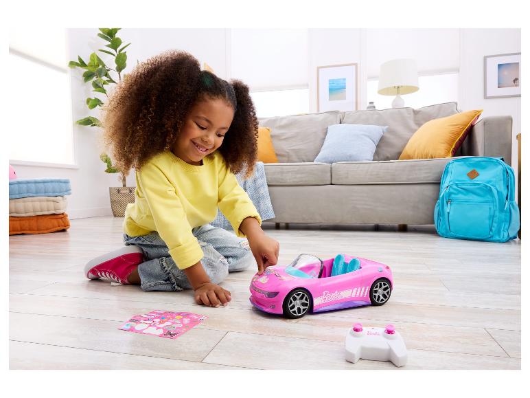 Lächelndes Mädchen verziert rosa Spielzeugauto mit Aufklebern, Fernbedienung daneben.