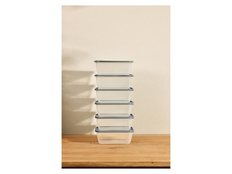 Stapel transparenter Lebensmittelbehälter mit grauen Deckeln auf einer Holzplatte.