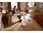 Ein weißer Saugroboter reinigt den Boden in einem modernen Wohnzimmer mit einem Mann am Schreibtisch.