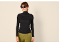 Frau in schwarzem Rollkragenpullover, grüner Hose und Sonnenbrille.