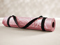 Eine rosa Yogamatte mit Muster und schwarzem Tragegurt.
