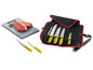 Ein Messerset mit gelben Griffen in einer Rolle, neben einem Schneidebrett mit zwei Steaks.