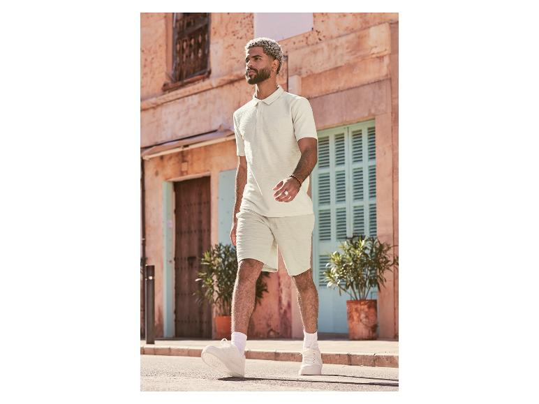 Mann in weißem Poloshirt und Shorts geht auf der Straße.