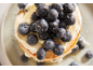 Nahaufnahme von Pfannkuchen mit Sahne, Blaubeeren und Honig auf einem Teller.