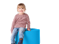 Lächelndes Mädchen sitzt auf einem blauen Hocker, trägt rosa Pullover und Jeans.