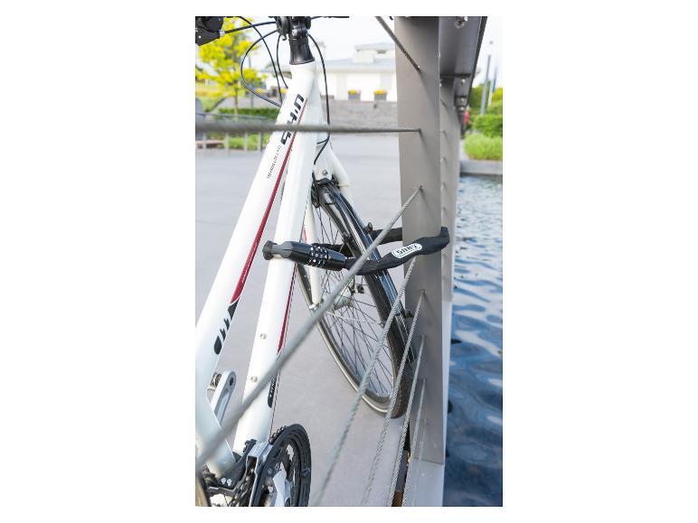 Weißes Trekkingrad mit schwarzem Schloss an einem Metallgeländer über Wasser gesichert.