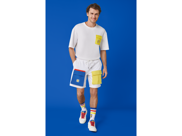 Mann in weißem T-Shirt, weißen Shorts mit farbigen Taschen und Turnschuhen.