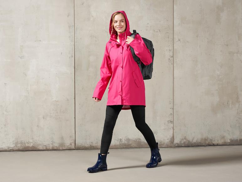 Eine Frau in einem rosa Regenmantel und blauen Gummistiefeln mit einem Rucksack.