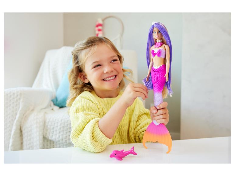 Lächelndes Mädchen spielt mit einer Meerjungfrauenpuppe und einem rosa Delfinspielzeug.