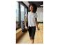 Frau in weißem T-Shirt und schwarzen Capri-Leggings, mit Tasche und Wasserflasche.