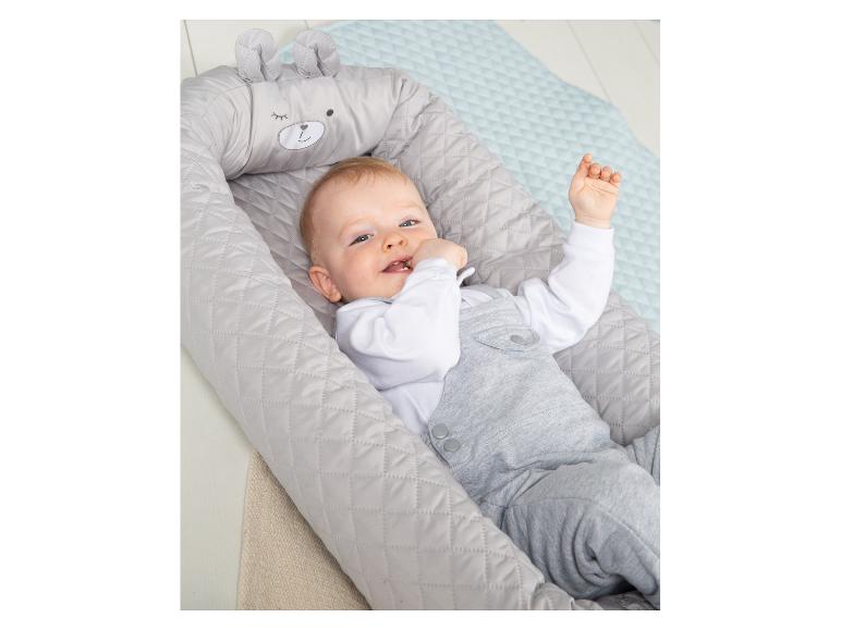 Glückliches Baby in einem grauen Babynest mit Bärengesicht und Ohren, liegend auf einer hellblauen Decke.