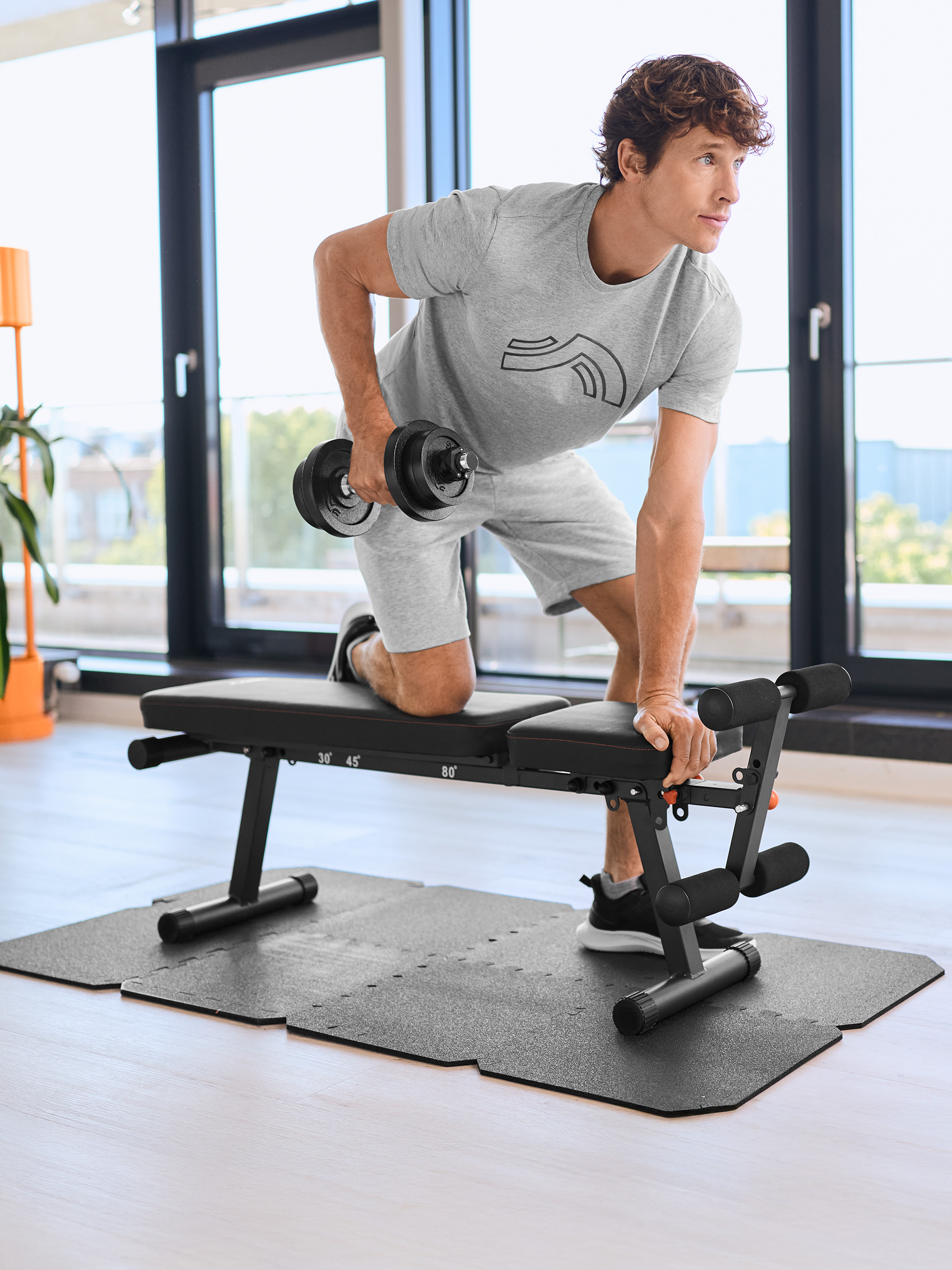 Mann trainiert mit einer Hantel und einer Hantelbank auf einer Trainingsmatte.
