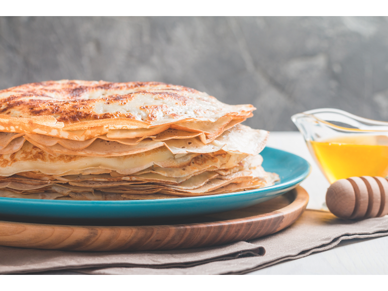 Stapel Pfannkuchen auf blauem Teller mit Honig und Honiglöffel aus Holz.