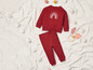 Ein rotes Sweatshirt mit Regenbogen und passende Hose auf einer weißen Decke.