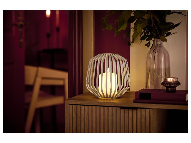 Eine weiße Laterne mit Kerze und eine Vase mit Grünpflanzen auf einem Holzschrank.