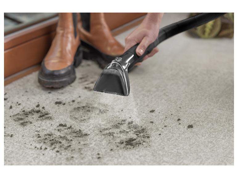 Eine Person reinigt einen schmutzigen Teppich mit einem Teppichreiniger, braune Stiefel tragend.