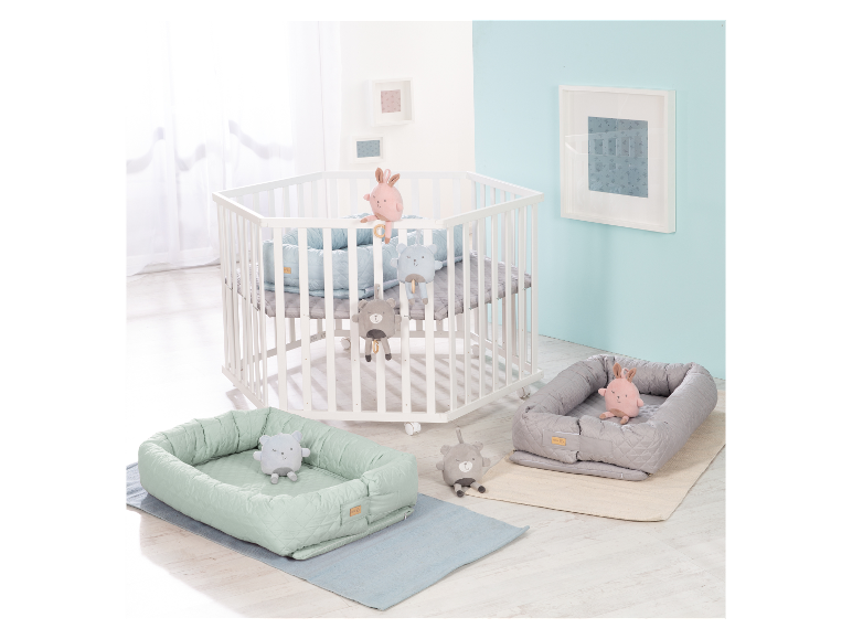 Weißes sechseckiges Babybett mit Matratzen und Plüschtieren.