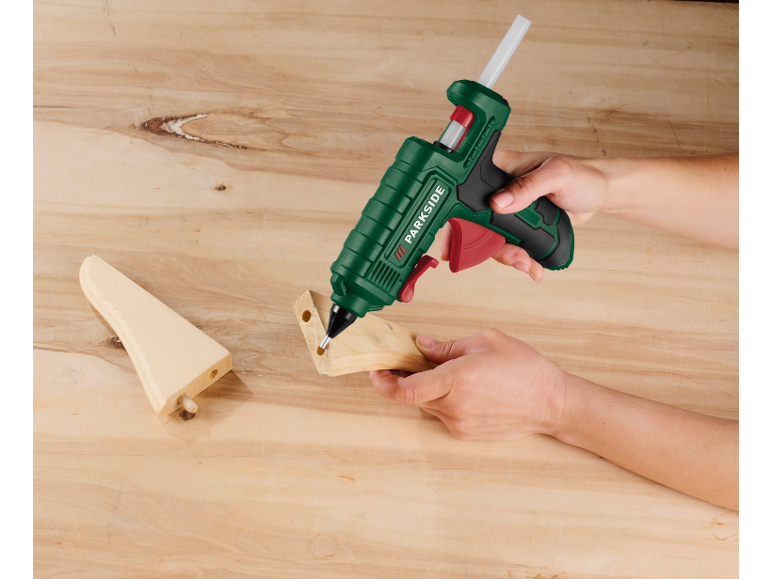 Hand benutzt Heißklebepistole an Holzteilen auf einem Holztisch.