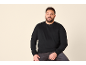 Mann in schwarzem Sweatshirt und Jeans, lächelnd.