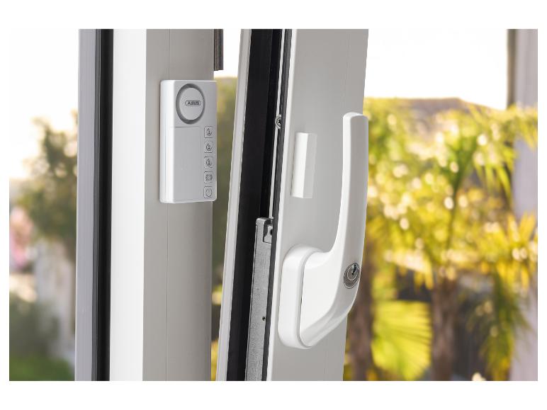 Weißes Fenster mit Alarmanlage und Griff mit Schloss, vor verschwommenem grünem Hintergrund.