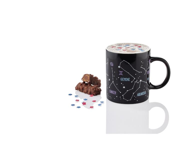 Eine schwarze Tasse mit Sternbildern, Schokoriegel und sternförmigen Streuseln.
