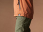 Eine orange Softshelljacke mit grüner Hose.