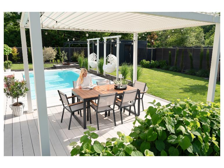 Frau liest an einem Esstisch auf einer Terrasse am Pool mit Pergola.