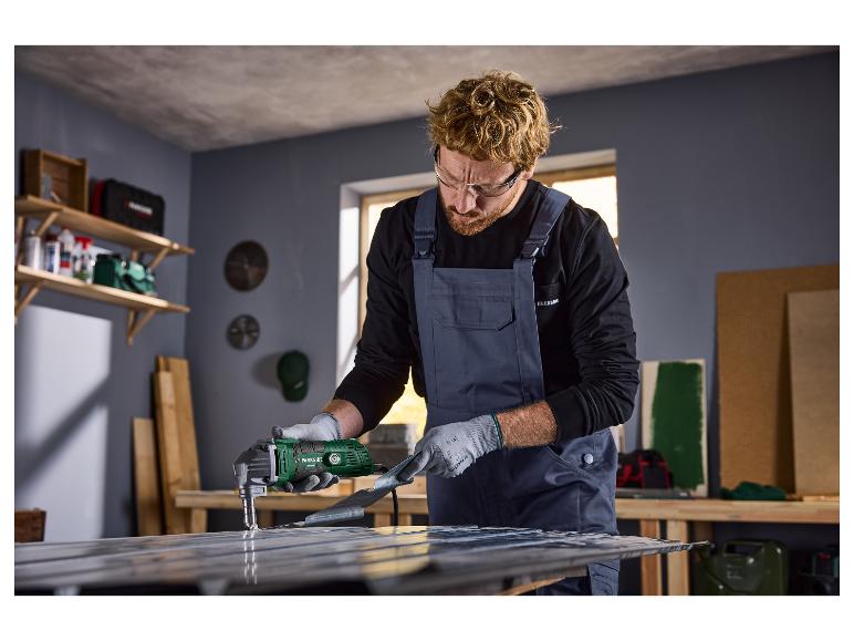 Mann mit Schutzbrille und Overall benutzt eine Parkside elektrische Blechschere auf einem Metallblech.