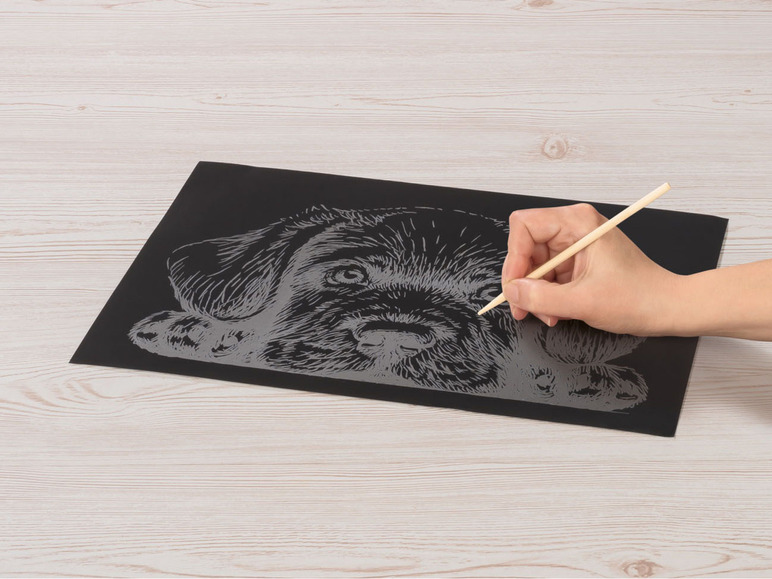 Eine Person kratzt ein Bild eines Welpen auf einem schwarzen Papier.
