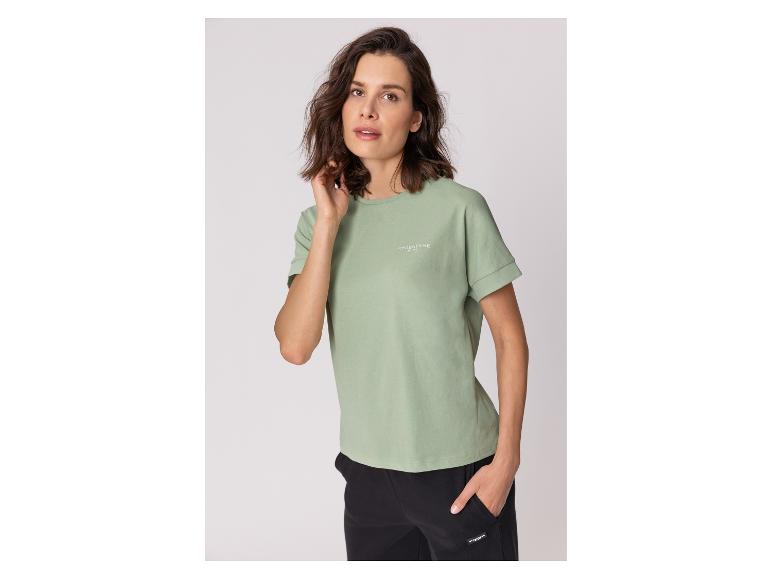 Frau in hellgrünem T-Shirt und schwarzer Hose, mit Hand in der Tasche.
