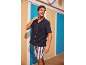Mann in einem marineblauen Kurzarmhemd und gestreiften Shorts, lächelnd in einer Strandhütten-Umgebung.
