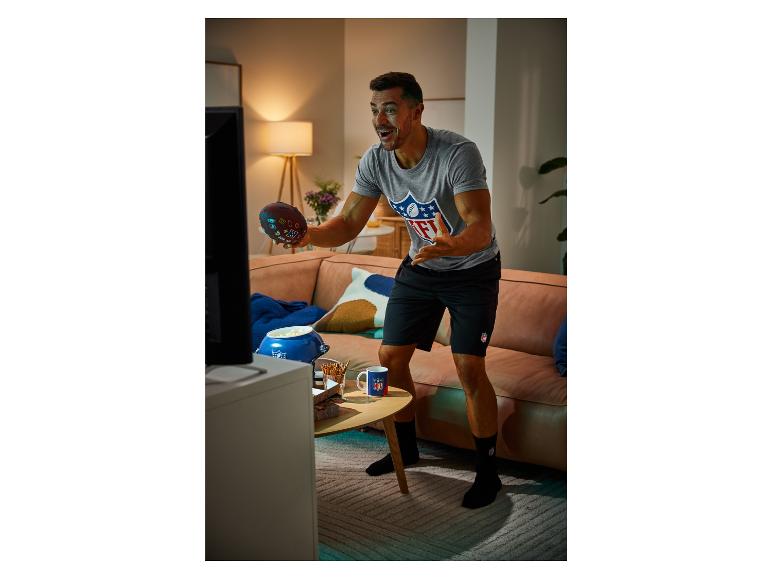 Mann mit NFL-Shirt, Socken und Tasse wirft einen Football in die Luft.