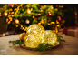 Leuchtende Weihnachtskugeln auf einem Teller mit Tannenzweigen vor dem Baum