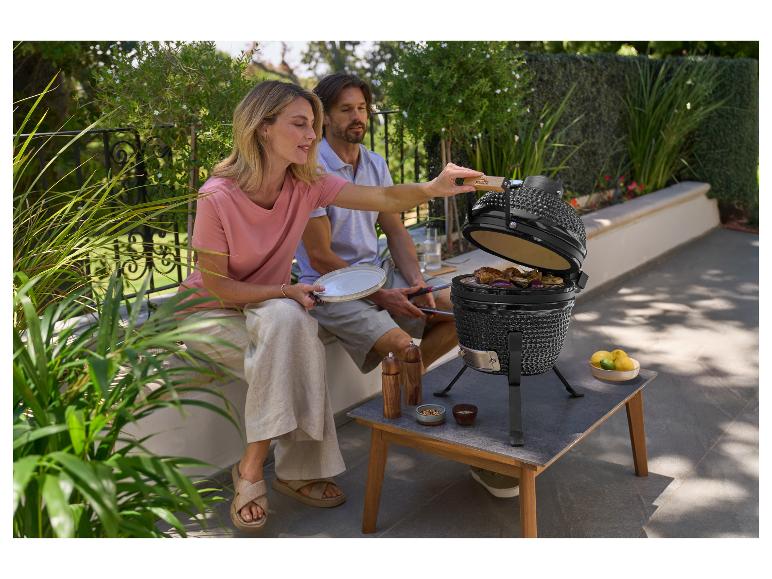 Ein Paar grillt Fleisch und Gemüse auf einem Kamado-Grill im Freien.