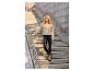 Frau in beigem Cardigan und schwarzen Kunstleder-Leggings auf Betontreppe.