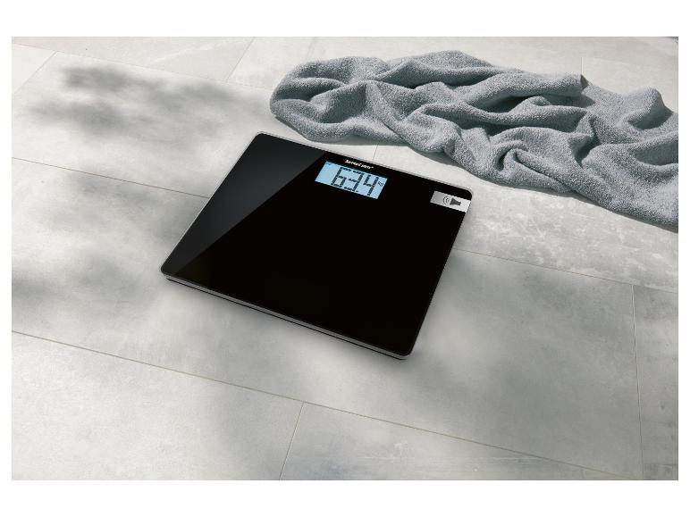 Schwarze SilverCrest Personenwaage mit Digitalanzeige und Handtuch.