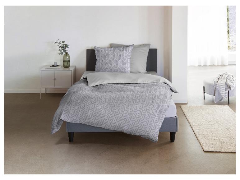 Schlafzimmer mit Bett, grauer gemusterter Bettwäsche, Nachttisch und Hocker.