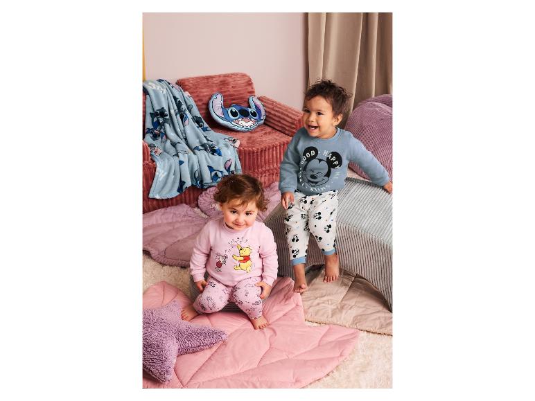 Zwei Kleinkinder in Pyjamas, eines in Rosa mit Winnie Puuh, das andere in Blau mit Mickey Maus.