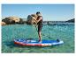 Mann auf blau-rotem aufblasbarem Paddleboard in klarem Wasser, Felsen im Hintergrund.