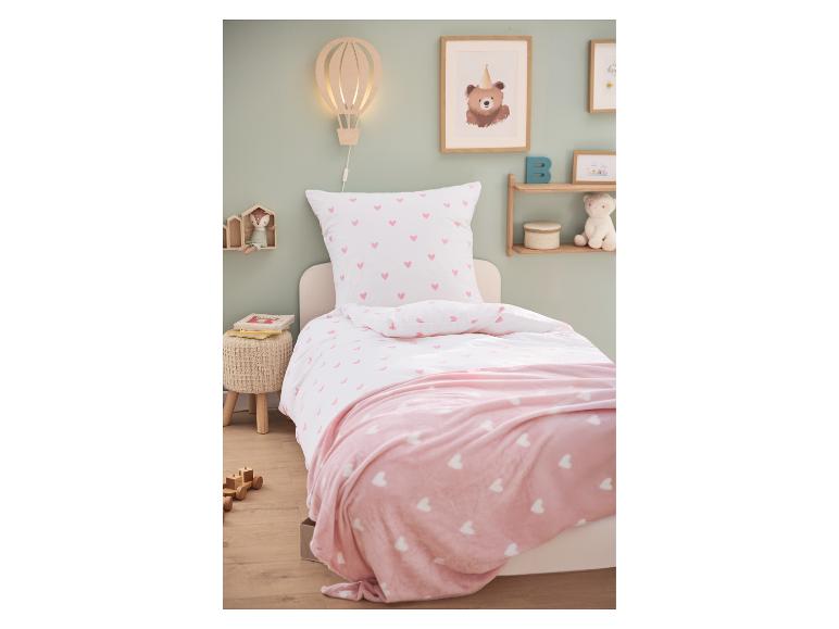 Kinderbett mit weißer Bettwäsche mit rosa Herzen und rosa Decke