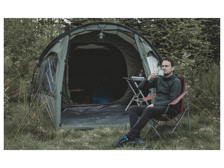 Ein Mann sitzt auf einem Klappstuhl vor einem grünen Zelt und trinkt aus einer Tasse.